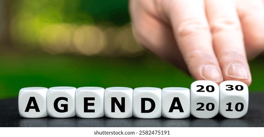 Hand turns dice and changes the expression 'agenda 2010' to 'agenda 2030'.