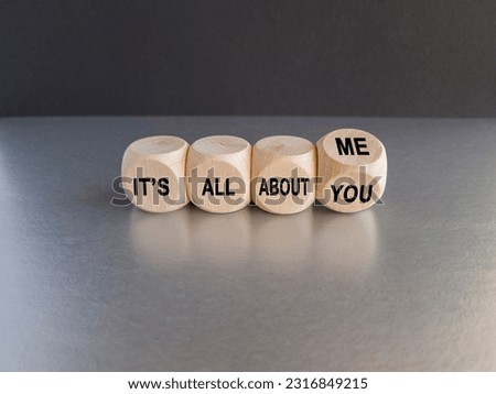 Hand turns dice and changes the expression 'it's all about you' to 'it's all about me'. Beautiful grey table, black background. Copy space.