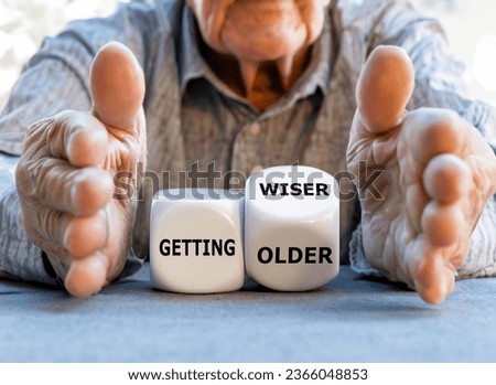 Hand turns dice and changes the expression 'getting older' to 'getting wiser' in front of an old man.	