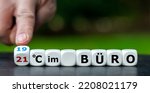 Hand turns dice and changes the German expression "21 Grad im Buero" (21 degrees in the office) to "19 Grad im Buero" (19 degrees in the office). 
