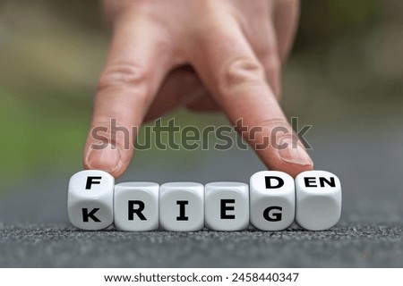 Hand turns dice and changes the German word 'Krieg' (war) to 'Frieden' (peace).