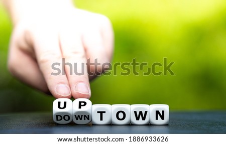 Hand turns dice and changes the word downtown to uptown.