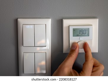 Hand turns down the temperature to 19 degrees Celsius on a electronic thermostat. Symbol for saving energy. - Shutterstock ID 2208318127