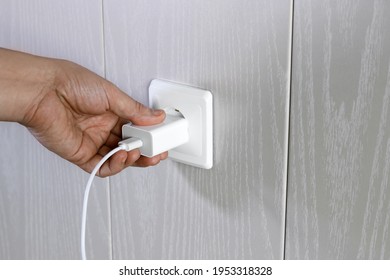 Hand Turns On, Turns Off Charger In Electrical Outlet On Wall, Close-up With Copy Space