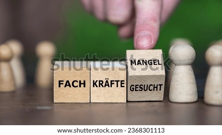 Hand turns wooden cube and changes the German expression 'Fachkraefte gesucht' (skilled workers wanted) to 'Fachkraeftemangel' (skilled workers demand).