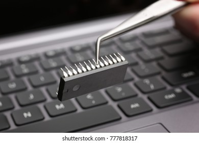 Hand With Tweezers Holds The Chip Above The Keyboard Of The Laptop