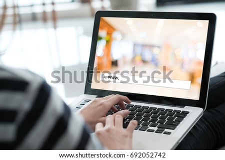 Hand tying labtop computer with www. on search bar over blur store background on screen, on line shopping ,business, E-commerce, technology and digital marketing background