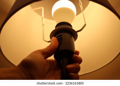 a hand under a lighted lamp shade with its thumb on the black switch to turn off the light