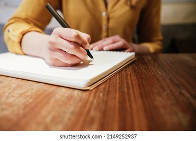 hand of an unrecognizable caucasian young woman writing with a pen on a paper notebook
