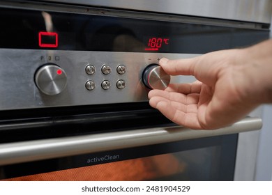 Hand of an unrecognizable person using the temperature selector of an oven in the kitchen of his home to preheat and then bake.