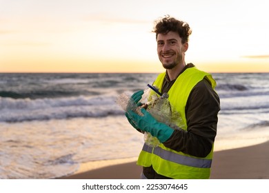 Hand of an unrecognizable volunteer picking up bottle from the ground on a beach at sunset. Environmental concept. Wearing vest and gloves. - Powered by Shutterstock