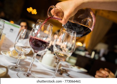 Hand of unrecognizable waiter pouring red wine to glass in restaurant. 