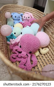 The Hand Of An Unrecognizable Young Woman Close-up Selects A Baby Toy From A Straw Cradle. The Girl Takes A Toy In Her Hand. Knitted Toys Large Octopuses Lie In A Straw Basket. We Choose A Gift In A