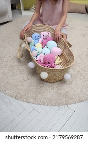 The Hand Of An Unrecognizable Young Woman Close-up Selects A Baby Toy From A Straw Cradle. The Girl Takes A Toy In Her Hand. Knitted Toys Large Octopuses Lie In A Straw Basket. We Choose A Gift In A