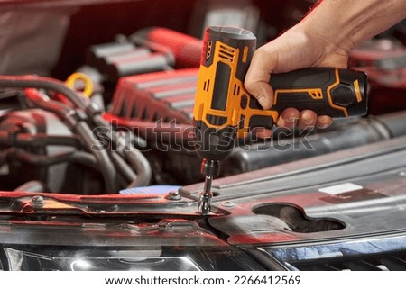 a hand unscrews a nut with a yellow battery wrench from a car