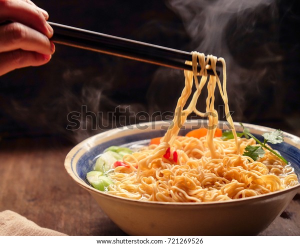 Hand\
uses chopsticks to pickup tasty noodles with\
smokes.