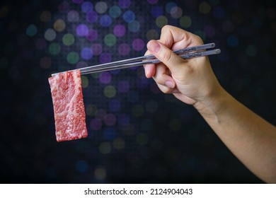 Hand using chopsticks to pick up wagyu beef, Raw wagyu beef over black background.