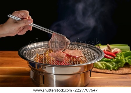 Hand using chopsticks to pick up wagyu beef on hot charcoal Asian BBQ food style, Grilled Beef Sirloin meat on the charcoal stove,Korean BBQ style.