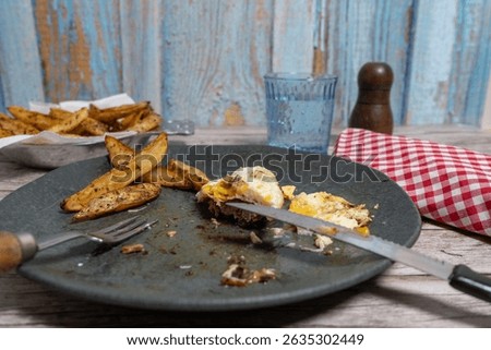 Hand using cutlery to cut into a hamburger steak on a dirty plate with fries and a fried egg, ready to eat