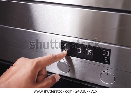 A hand is using a finger to activate the timer button on the control panel of a stainless steel oven