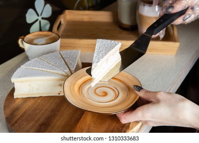 A hand using a kitchen spatula picks up one of five pieces of cheesecake from a wooden tray