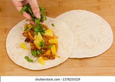 Hand using knife to cut pineapple slices and limes on a wooden cutting board background.