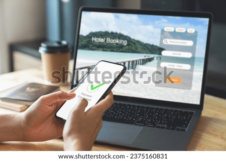Hand using laptop and booking hotel on website for vacation after a long work and payment completed message on mobile, Summer holiday concept.