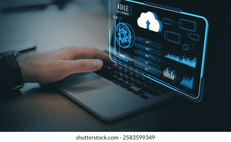 Hand using laptop with a virtual holographic interface displaying agile development data and cloud upload icon on wooden desk background