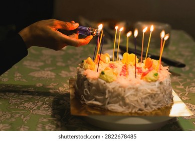 Hand using a lighter to light candles on white coconut birthday cake