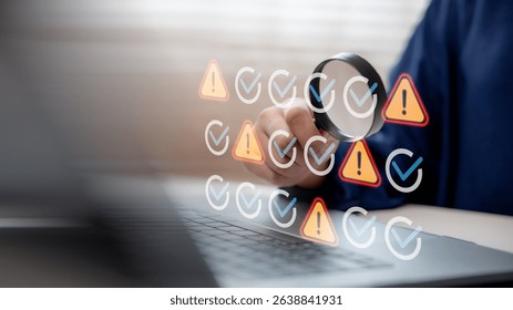 Hand using magnifying glass to inspect warning and check icons on laptop screen, representing system monitoring, debugging, error detection, and cybersecurity analysis.
