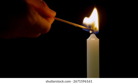A hand is using a match to ignite a mourning candle wick in a dark setting, creating a warm and flickering flame.