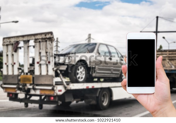 Hand\
using mobile smartphone for emergency roadside service with Broken\
car on tow truck after traffic accident\
background