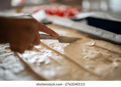 Hand using an offset spatula spreading cream onto a sheet of cake batter in a baking pan, preparing a sweet dessert