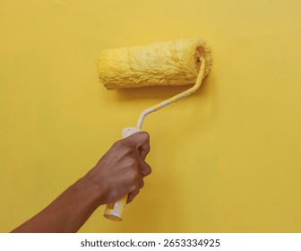 A hand using a paint roller to apply yellow paint on a wall, perfect for home improvement, renovation, construction, and DIY project illustrations.