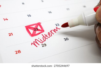 Hand Using a Red Marker to Circle an Important Midterm Exam Date on a Calendar, Signifying Academic Deadlines and Planning