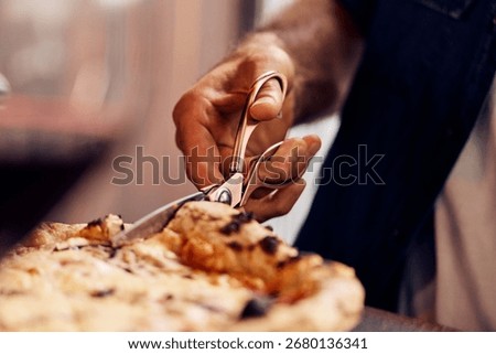 Hand using scissors to cut freshly baked pizza, depicting culinary creativity and style.