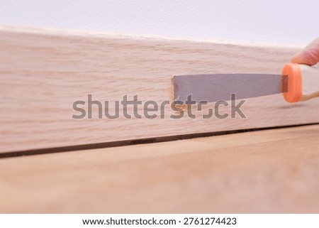 Hand using a scraper to smooth wood filler on an oak skirting board