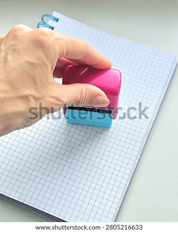 Hand Using a Self-Inking Stamp on a Grid Notebook