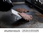 Hand using a spatula to flip cooking smash burgers on a grill in a restaurant kitchen