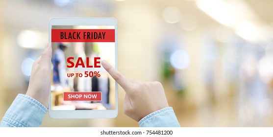 Hand using tablet with black friday online sale on screen device over blur store background with copy space, business and technology, online shopping, digital marketing concept