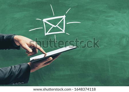 Hand using tablet with drawing e-mail symbol on green blackboard background. Business and media concept.
