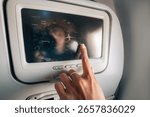 Hand using touchscreen on airplane to check flight route over map