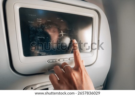 Hand using touchscreen on airplane to check flight route over map