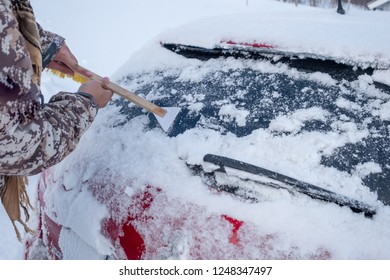 Hand using web scraping snow on car rear windscreen in winter