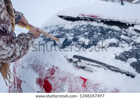 Hand using web scraping snow on car rear windscreen in winter