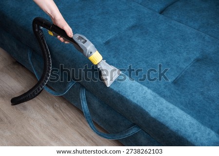 Hand using wet vacuum cleaner on blue fabric sofa, showing deep cleaning of upholstery, effective removal of dirt and stains, refreshing home furniture fabric.