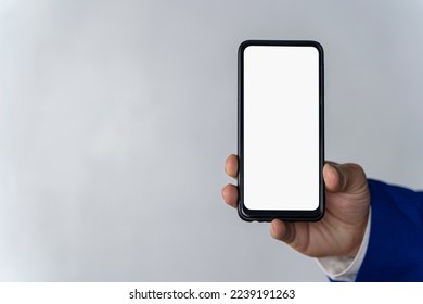 Hand using white smartphone screen on gray surface background, close-up top view. Smartphone with a white screen in businessman's hand.