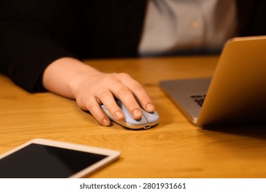 Hand using wireless mouse next to laptop on wooden desk