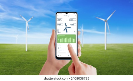 Hand utilizes a wind generator app to monitor energy production. Meadow with spinning wind generators in background