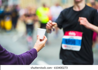 Hand Of A Volunteer Giving A Cup Of Water At A Refreshment Point In A Marathon Race To Runners.